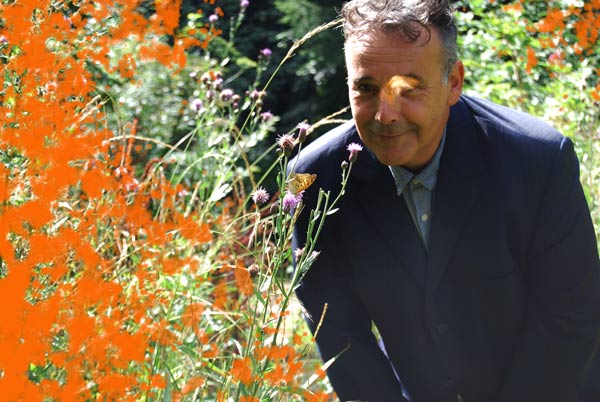 Rob Newman smiling in a wild garden, a butterfly in flight obscures part of Rob's face